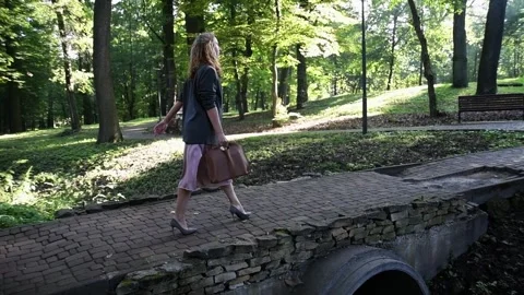 Slow motion back view of a young blonde woman walking through a park. Vídeos de archivo 333070401