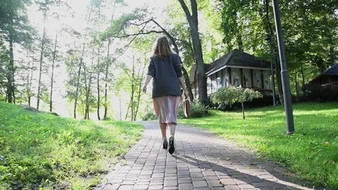 Slow motion back view of a young blonde woman walking through a park. Vídeos de archivo 333070432