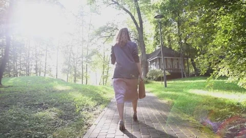 Slow motion back view of a young blonde woman walking through a park. Vídeos de archivo 333070433