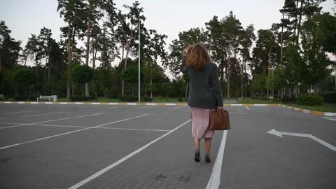 Slow motion back view of a young blonde woman walking across an empty parking 库存影片 333070808