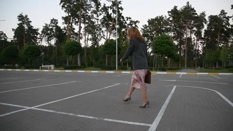Slow motion back view of a young blonde woman walking across an empty parking Vídeos de archivo 333070850