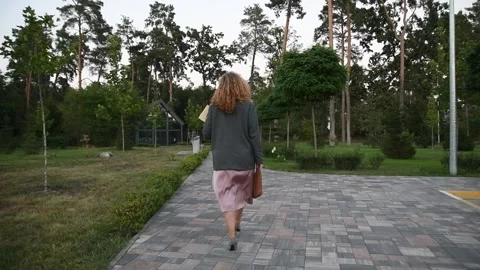 Slow motion back view of a young blonde woman walking through a park. Vídeos de archivo 333070893