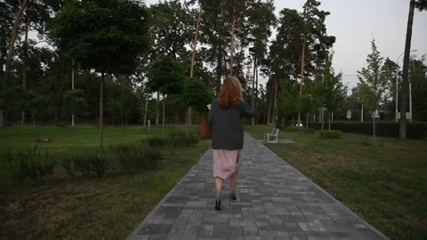 Slow motion back view of a young blonde woman walking through a park. Vídeos de archivo 333070976