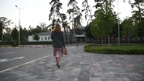 Slow motion back view of a young blonde woman walking across an empty parking Vídeos de archivo 333070979