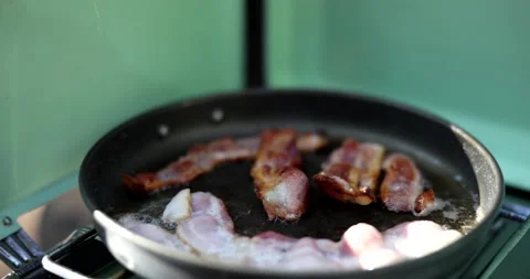 Slow motion of bacon frying in a pan on a camp stove Stock Footage 143659077