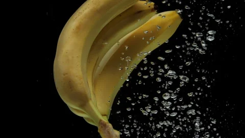 Slow motion bananas falling into transparent water on black background Stock Footage 269517949