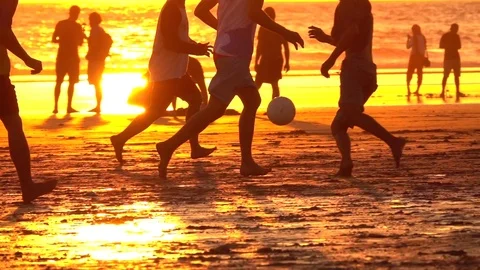 SLOW MOTION: Barefooted youngsters playing football on sandy beach at sunset Stock Footage 79978401