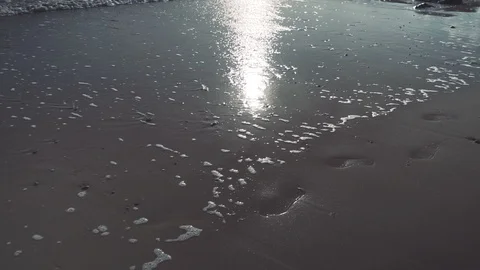 Slow motion beautiful walking shot as waves lap sandy beach with footprints Stock Footage 119533955