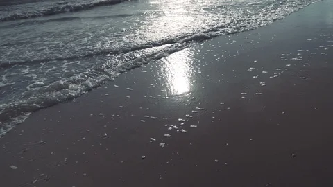 Slow motion beautiful walking shot as waves lap sandy beach with sun reflection Stock Footage 119534130