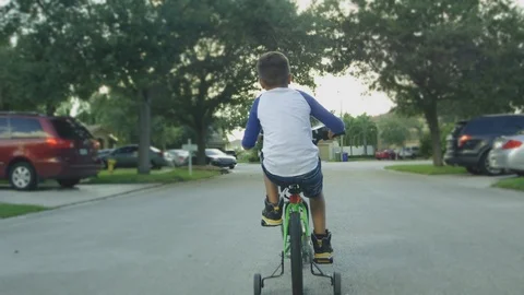 Slow motion from behind of kid riding a bike in a neighborhood street Stock Footage 92189621