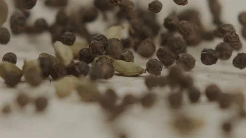 Slow motion black scented pepper peas falling on white table Stock Footage 113550994