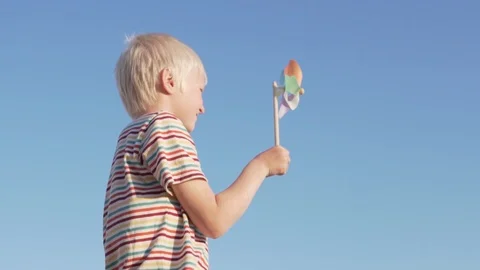 Slow motion a blond boy a spinning wind toy and joyfully smiles Stock Footage 108023137