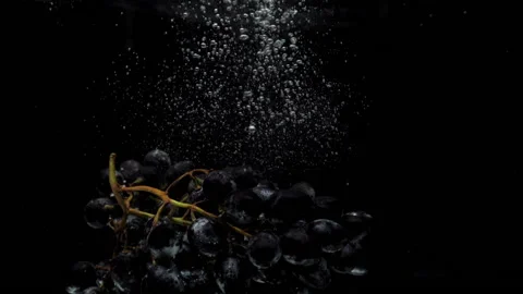 Slow motion blue grapes falling into transparent water on black background Video stock 163241857