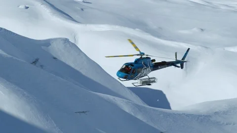 Slow motion of blue helicopter flying above snowy mountains during sunny day Stock Footage 129128034