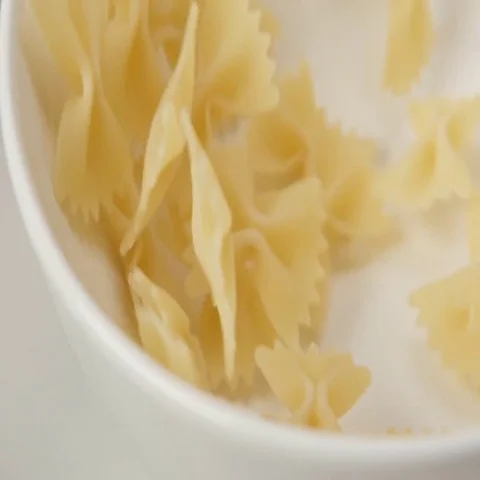 SLOW MOTION: Bow pasta fall on white dish (close up) Stock Footage 69477254