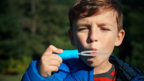 Slow motion of boy blowing soap bubbles on a lawn against of a green forest Stock Footage 91557805