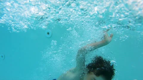Slow motion of boy jumping and splashing into a blue swimming pool underwater Stock Footage 344669599