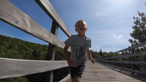 Slow motion of a boy running forward across a wood bridge Video stock 114105595
