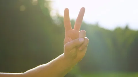 SLOW MOTION: Bright sunbeams shine on male hand and showing the peace sign. Stock Footage 102533161