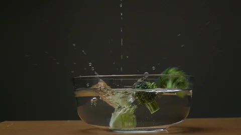 Slow motion of broccoli falling in to water splashing on black background. Stock Footage