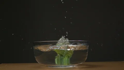 Slow motion of broccoli falling in to water splashing on black background. Stock Footage