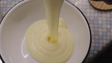 Slow motion, cake custard pouring into a white bowl on the kitchen counter Stock Footage 304694791