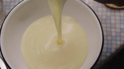 Slow motion, cake custard pouring into a metal bowl on the kitchen counter Stock Footage 304745392