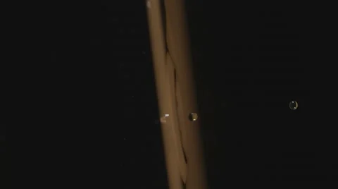 Slow motion, camera rotates as drop splashes to golden water surface in ripples Stock Footage 63846808