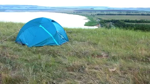 Slow motion camera view of a blue tent set up on the hilly grassy shore of th Stock Footage 135897513