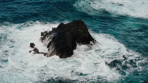 Slow-motion capture of waves powerfully crashing around a dark sea stack in Stock Footage 312030788