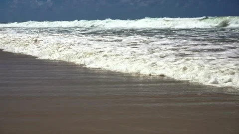 Slow motion captures powerful ocean waves crashing onto a sandy shore, breaking Stock Footage 306125816