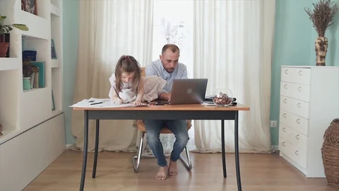 SLOW MOTION. A Caucasian man working online from home. A little girl gives a Stock Footage 129599386