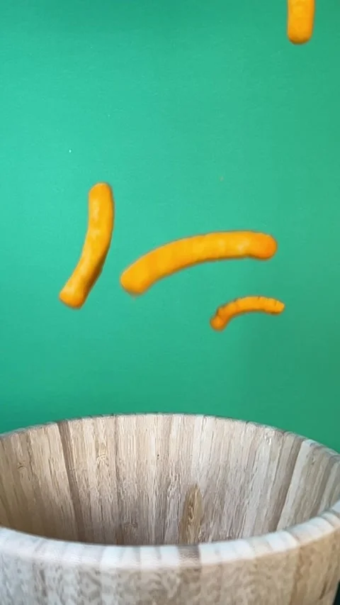 Slow motion of cheese puffs falling into a wooden bowl, vertical Stock Footage 345154374