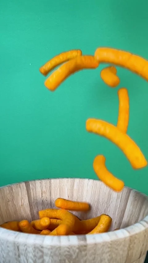 Slow motion of cheese puffs falling into a wooden bowl, vertical Stock Footage 345154518