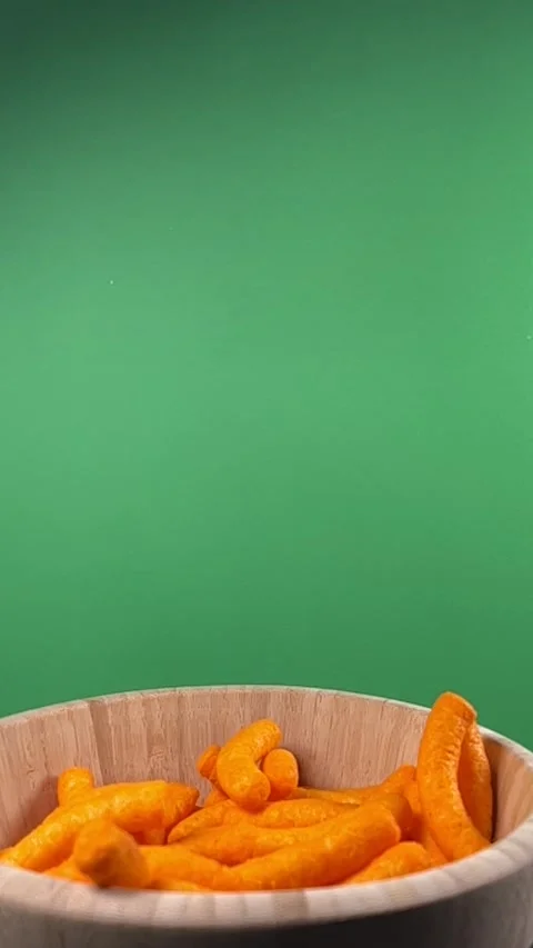 Slow motion of cheese puffs falling into a wooden bowl, vertical Stock Footage 345154525