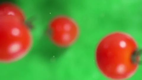 Slow motion of cherry tomatoes and water drops flying on green background. Stock Footage 309098052