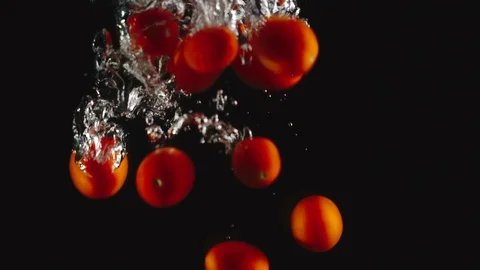 SLOW MOTION: Cherry tomatoes fall under water on black background Stock Footage 97914355