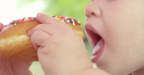 Slow Motion Child Takes a Bite of a Glazed Donut with Sprinkles Stock Footage 61468086