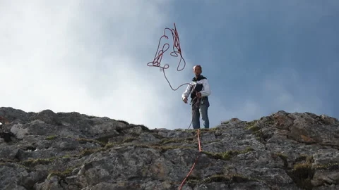 Slow motion of a climber throws a rope while standing on top of a mountain. Stock Footage 97601666