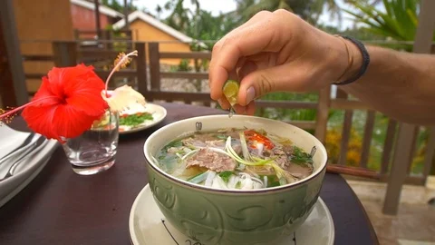 Slow motion clip of a man squeezing fresh lime into a Vietnamese noodle ramen Stock Footage 87857561