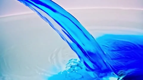A slow-motion clip shows blue liquid pouring into water against a white backdrop Stock Footage 320921077