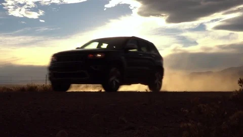 SLOW MOTION CLOSE UP Black SUV car driving on dusty dirt road at golden sunrise Stock Footage