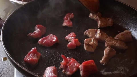 Slow motion close-up cooking small pieces of red meat in the pan with a wooden h Stock Footage 199580420