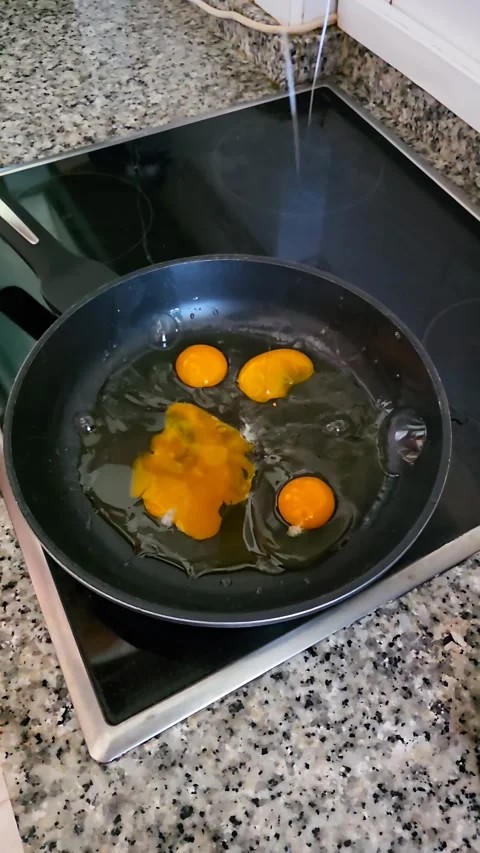 Slow motion close up of cracking eggs onto a hot frying pan on stove apo8 pr Stock Footage 338259876