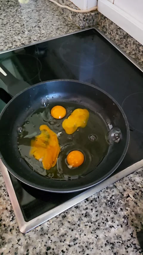 Slow motion close up of cracking eggs onto a hot frying pan on stove1 apo8 p Stock Footage 338259887