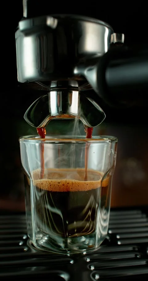 Slow motion close-up of espresso pouring from a coffee machine into a glass cup Видео 331263727