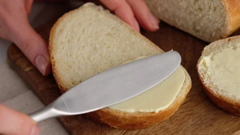 Slow motion. Close-up of female hands smear butter with a kitchen knife on a Stock Footage 146154691
