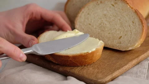 Slow motion. Close-up of female hands smear butter with a kitchen knife on a Video stock 146154739