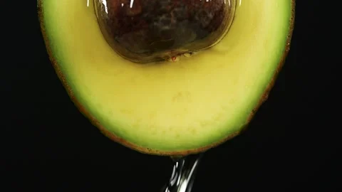 Slow motion close-up of fresh avocado fruit and oil flowing on black background Stock Footage 145471132