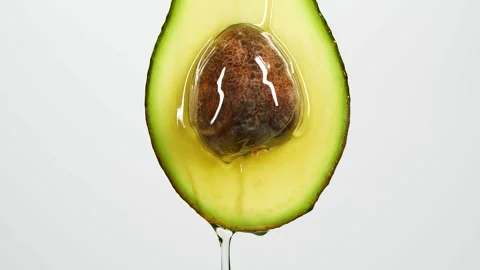 Slow motion close-up of fresh avocado fruit and oil flowing on white background Stock Footage 145471222